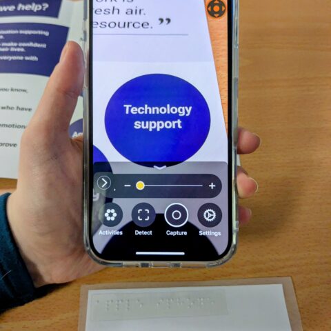 hand holding Apple iPhone magnifying a leflet on screen